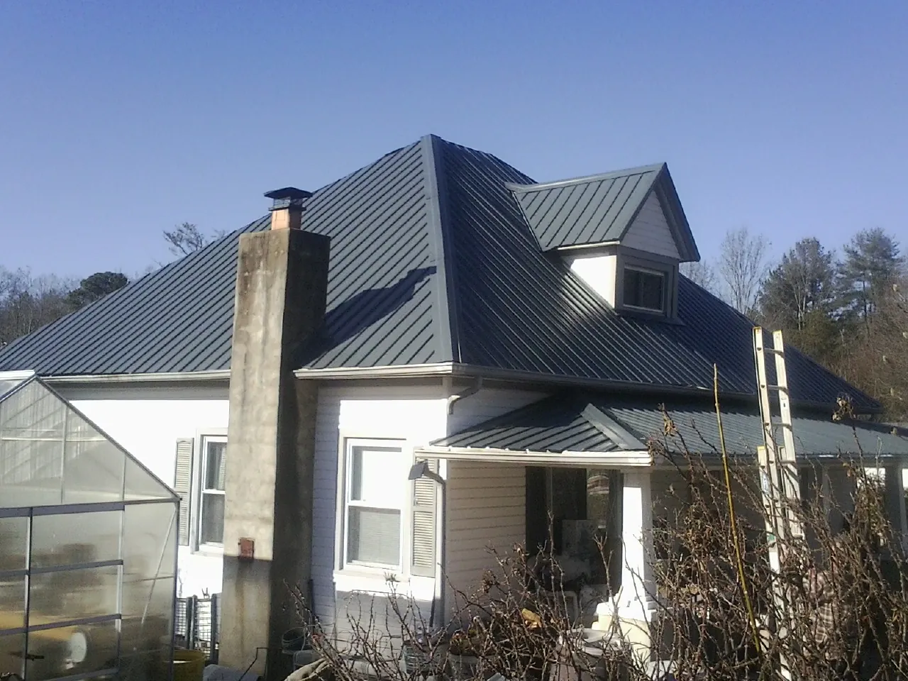 Dark blue standing seam metal roof on a white farmhouse with dormer — Slate & Tile Roof Repair by Roofing Brothers in Shaftsbury