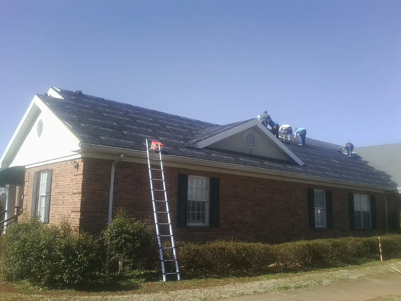 Crew tearing shingles off a brick ranch roof with a ladder set — Metal Roof Repair work by our crew in Shaftsbury