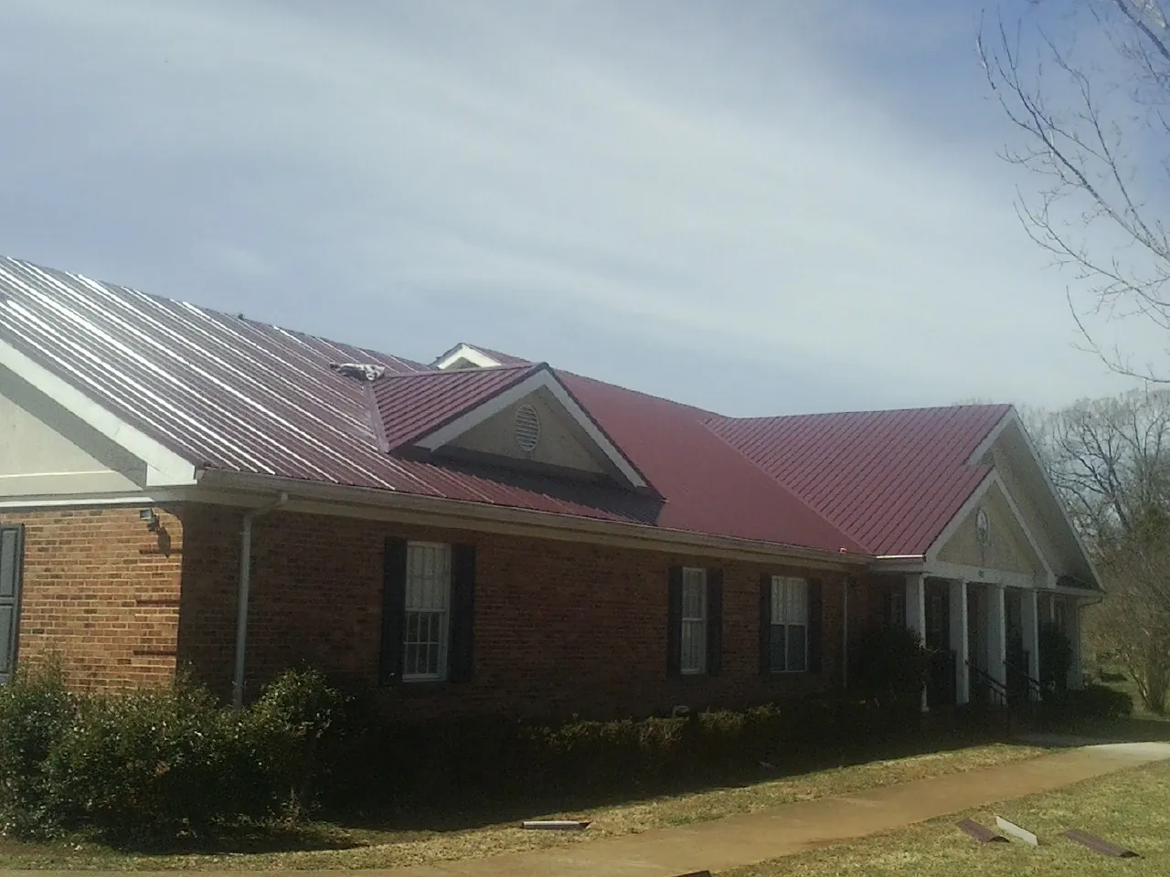 Red metal roof with gabled entries on a long brick building, from a Hail Damage Roof Repair job in Shaftsbury