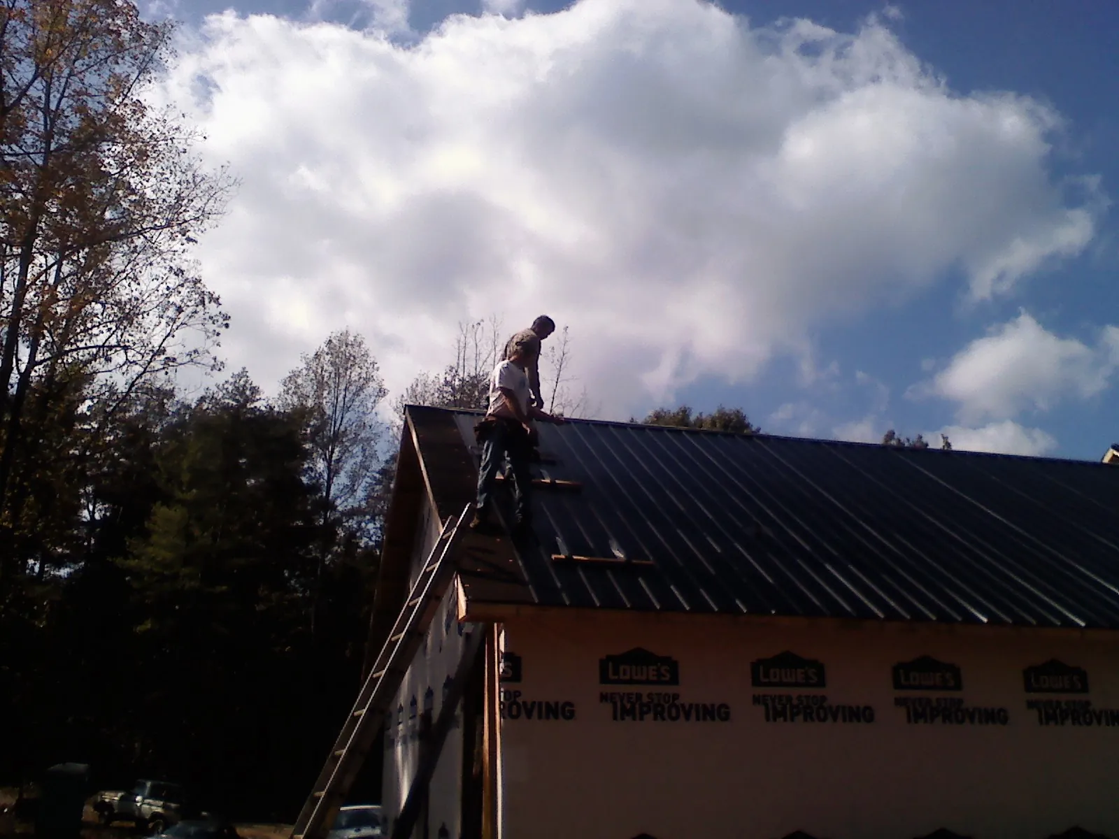 Roofer fastening dark metal panels high against a cloudy sky, from a Roof Inspection job in Shaftsbury