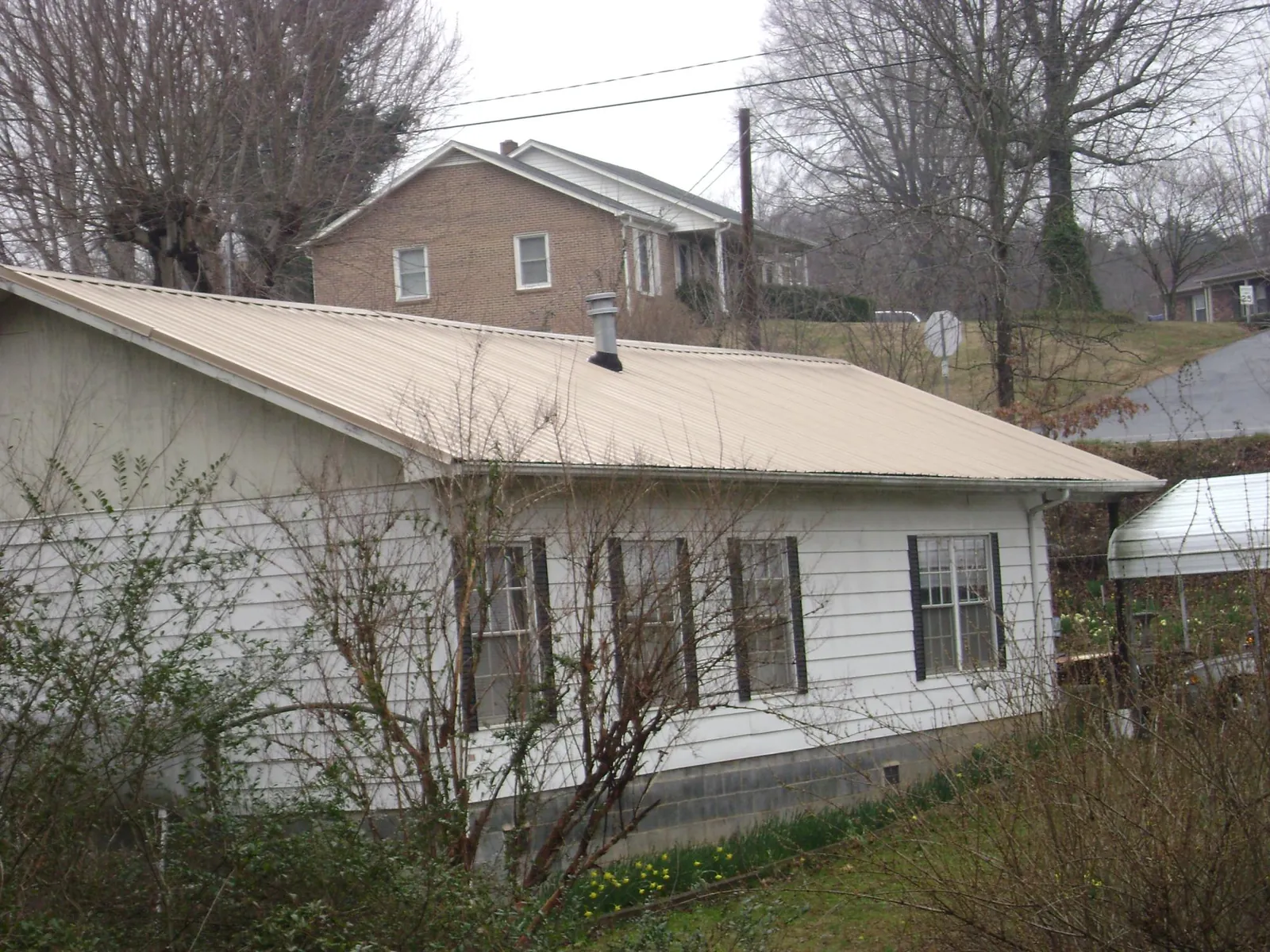 Tan metal roof on a white sided house set into a hillside — Commercial Roofing by Roofing Brothers in Shaftsbury